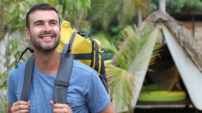 homem de mochila às costas com tenda por trás 