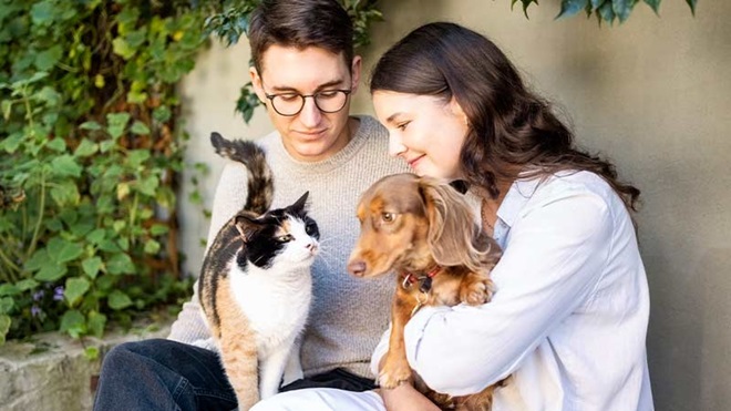 Casal com um cão e um gato ao colo, num quintal