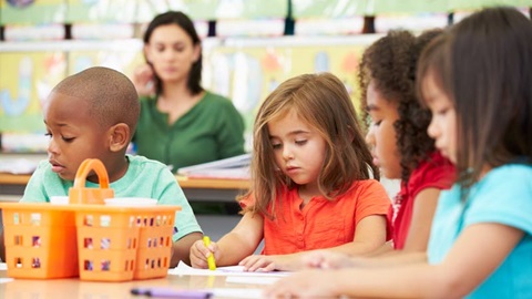 Crianças a fazer um desenho na escola, acompanhadas pela professora.