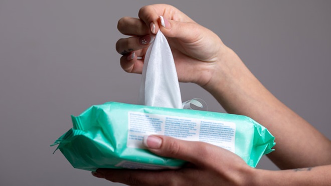 grade plano de mão de mulher a retirar uma toalhita de um pacote verde claro, fundo cinza