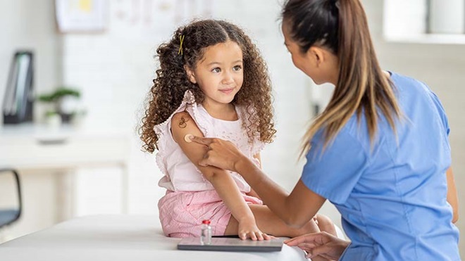 Enfermeira aplica algodão no braço de uma menina após toma da vacina.