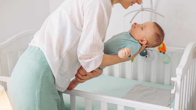 Mãe deita bebé no berço.