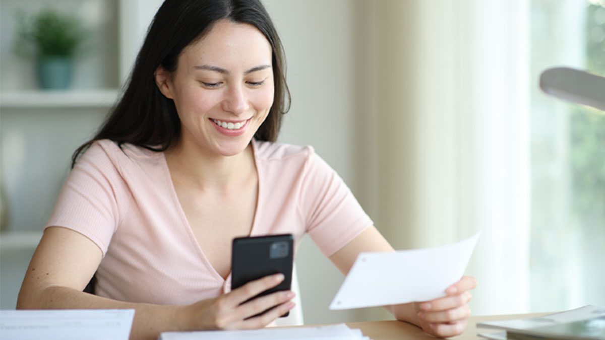 Mulher sorridente a consultar correspondência com telemóvel na mão