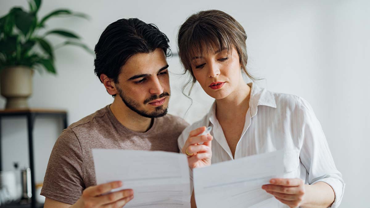 Casal com ar preocupado olha para uns documentos