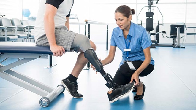 Homem sentado com prótese na perna, e fisioterapeuta