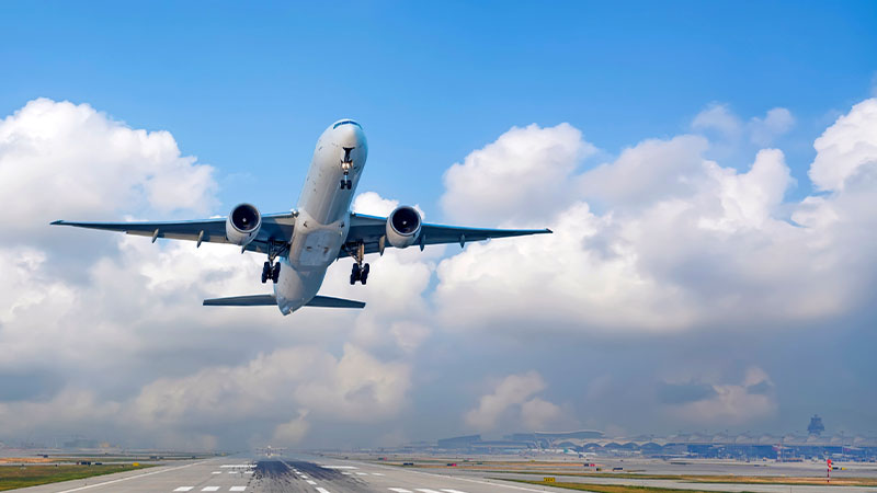 Avião a levantar voo num aeroporto, céu azul com nuvens