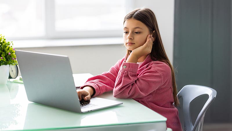 Criança sentada na secretária com computador portátil