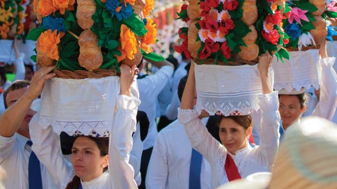 Mulheres carregam tabuleiros no cortejo na rua em Tomar com apoio de homens