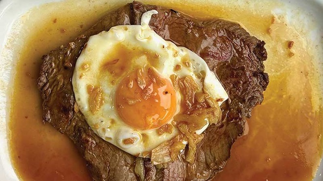 bitoque, bife de vaca com ovo estrelado e muito molho servido no prato em restaurante