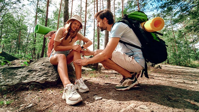 Casal em férias na natureza, com mochilas, mulher lesionada no joelho e homem a dar apoio