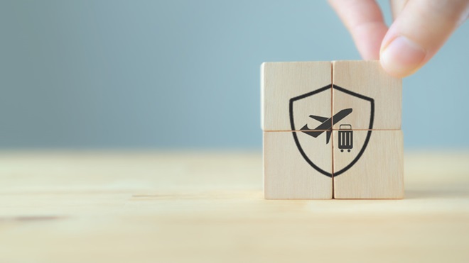 Mão a colocar a 4ª peça de madeira num conjunto de quatro que formam um símbolo de proteção com um ícone de viagem no interior