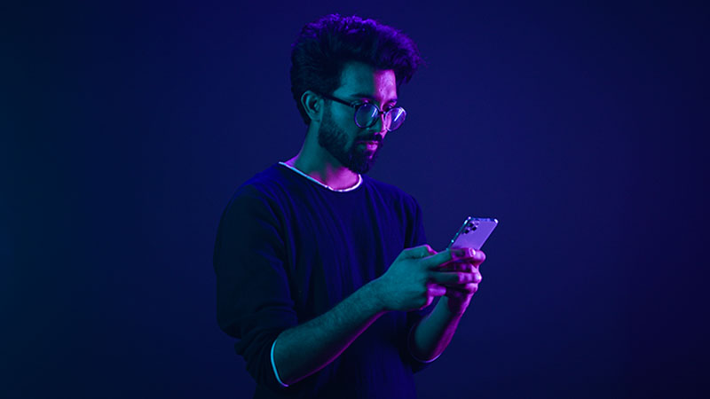 Adulto a pegar num telemóvel numa ambiente com cor azul roxeada - alusão a jogos online