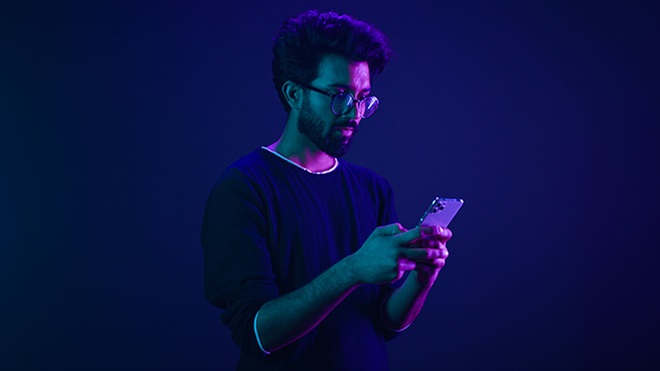 Adulto a pegar num telemóvel numa ambiente com cor azul roxeada - alusão a jogos online