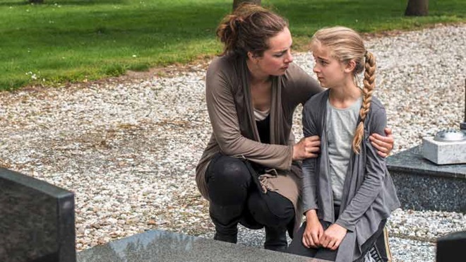 Mãe e filha pequena com ar triste, num cemitério