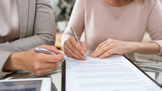 Duas pessoas a rever e assinar um documento sobre uma mesa, utilizando canetas prateadas