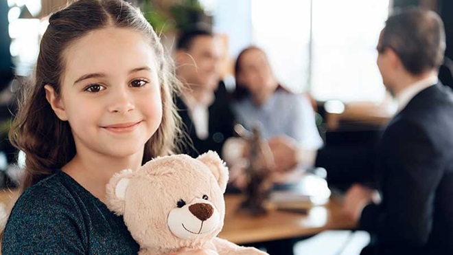 Criança com urso de peluche e três adultos ao fundo