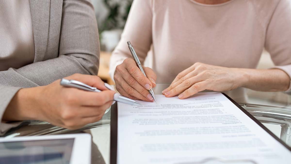 Duas pessoas a rever e assinar um documento sobre uma mesa, utilizando canetas prateadas