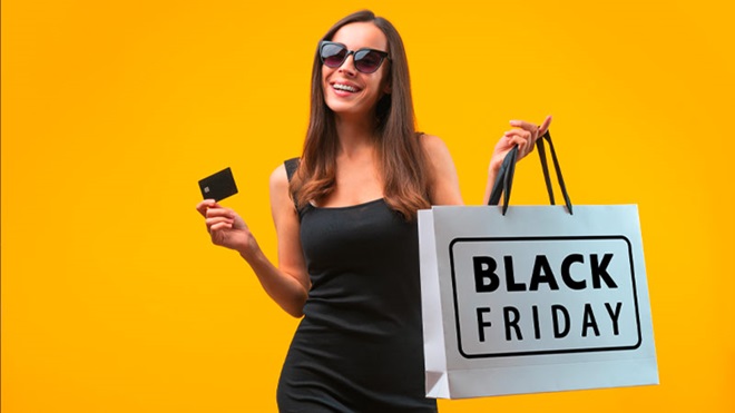 Mulher com vestido preto, cartão multibanco na mão, óculos de sol e um saco branco de papel a dizer black friday. Fundo amarelo