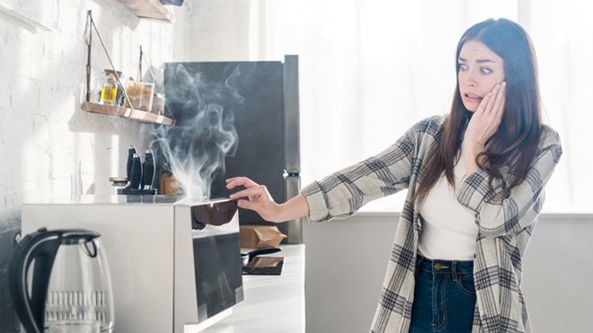 mulher na cozinha em pânico com micro-ondas a deitar fumo
