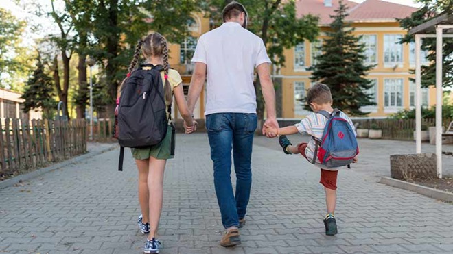 Criança com mochila a caminho da escola de mão dada com o pai
