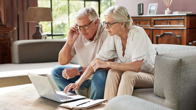 um casal de reformados sentado no sofá com um computador em frente