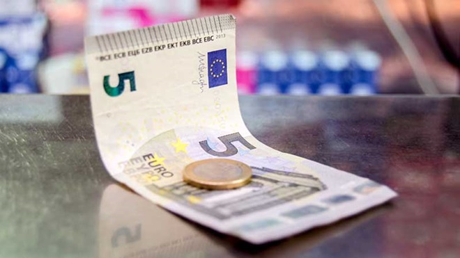 Nota de cinco euros com moeda de um euro em cima