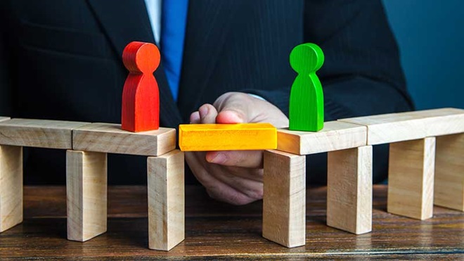 Homem a colocar uma ponte entre dois bonecos de madeira