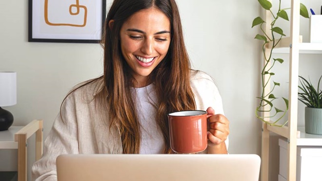 mulher a trabalhar no portátil com caneca na mão