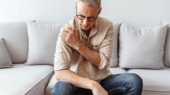 Homem sentado no sofá em casa com dores no ombro