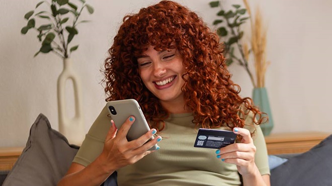 Mulher jovem a fazer compras online no telemóvel, com um cartão de crédito na mão