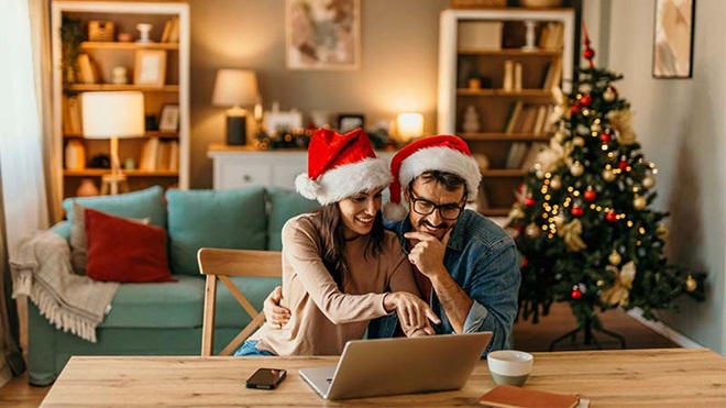 Casal com gorros de pai natal a usar computador portátil, numa sala com decoração de natal