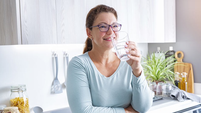 Senhora a beber água na cozinha