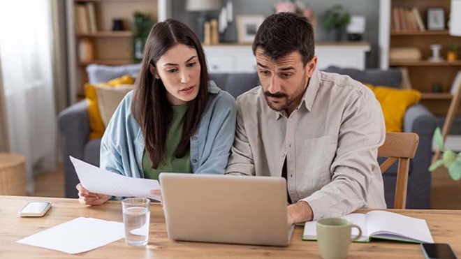 Casal com ar preocupado vê as suas contas e o computador