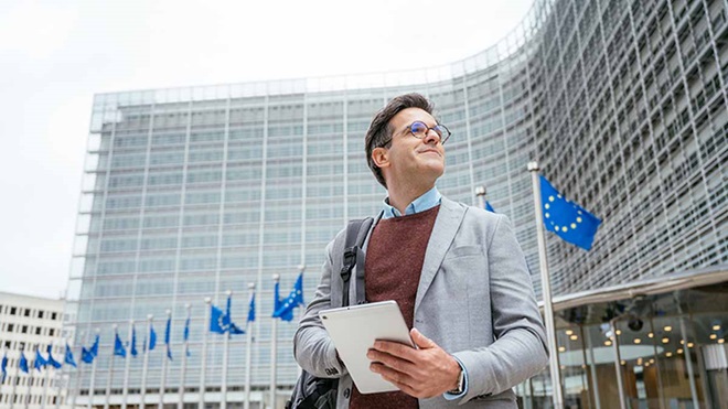 Homem com um tablet na mão em frente a um edifício com bandeiras da união europeia