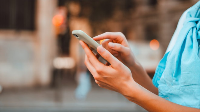 Grande plano de umas mãos a segurar um telemóvel e a mexer numa app - alusão à Plataforma Reclamar