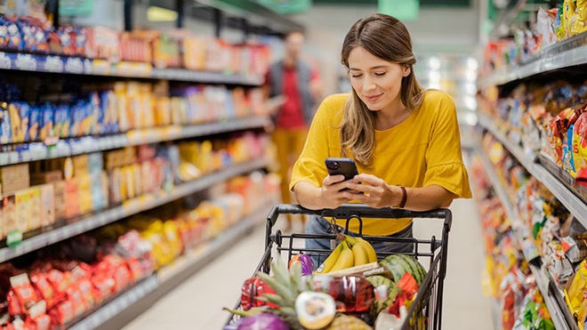 Rapariga com telemóvel às compras no supermercado