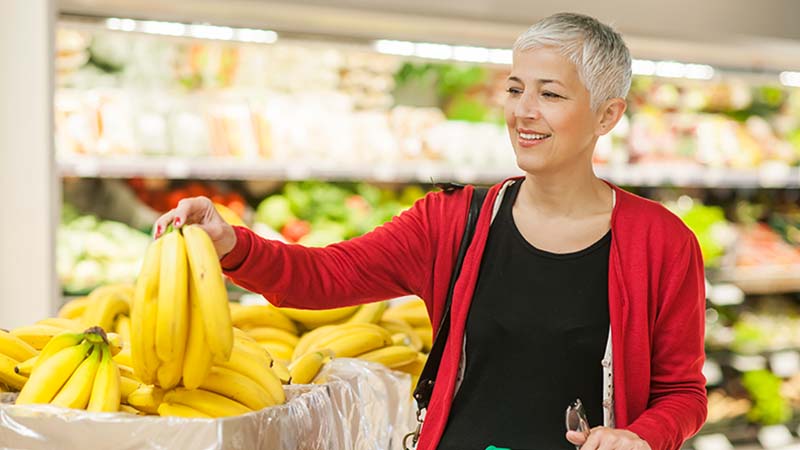 Mulher sénior a escolher um cacho de bananas no supermercado