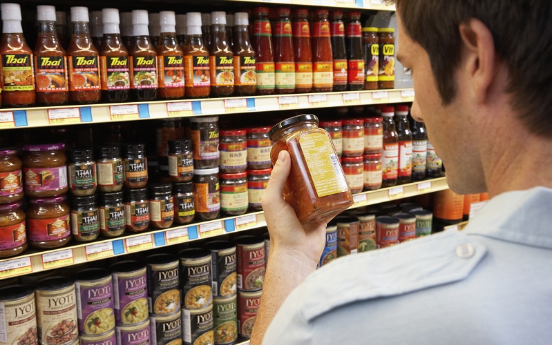 Homem no supermercado, a ler o rótulo de um frasco de comida.