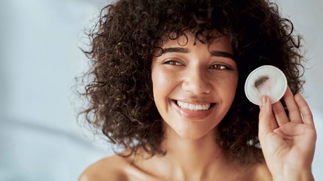 Mulher de cabelos encaracolados limpa o rosto com um disco de algodão