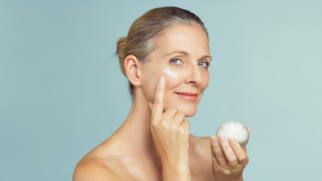 Mulher de meia idade a colocar creme antirrugas na pele do rosto