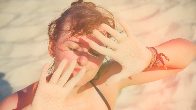Mulher exposta ao sol protege a cara dos raios solares; praia