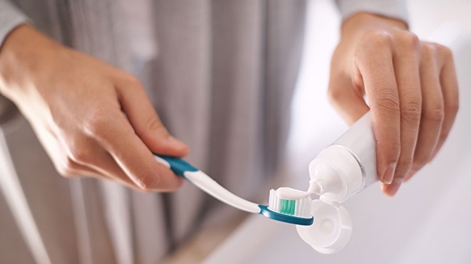 Mulher a colocar pasta dentífica na escova de dentes