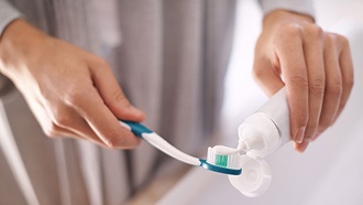 Mulher a colocar pasta dentífica na escova de dentes