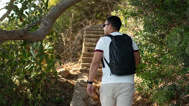 Homem de mochila às costas a passear numa mata junto à costa