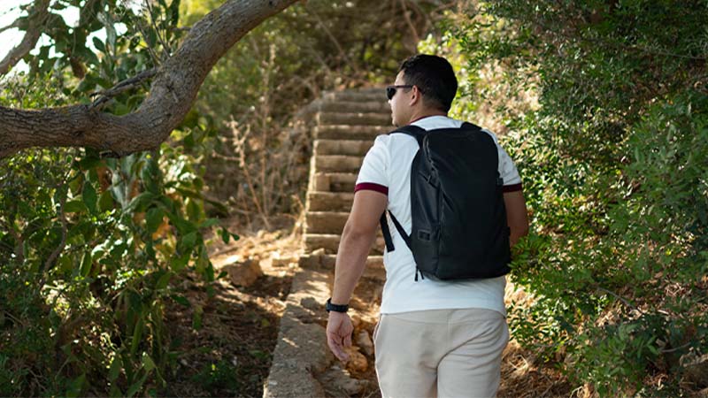 Homem de mochila às costas a passear numa mata junto à costa