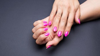 Grande plano de mãos de mulher com unhas de gel pintadas de rosa, sobre um fundo azul escuro