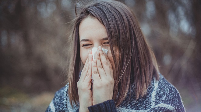 rapariga com alergia a assoar o nariz a um lenço de papel