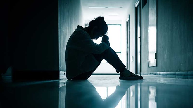 Rapariga sentada no chão com a cabeça apoiada nas mãos