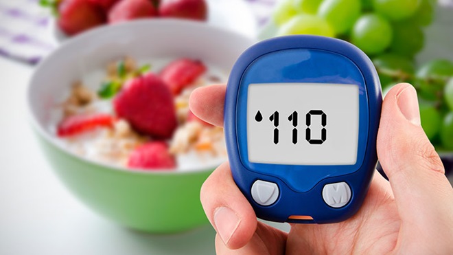 medidor de níveis de diabetes numa mão com taça de cereais e fruta ao fundo