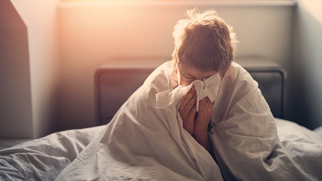 Rapaz enrolado no edredão, assoa-se